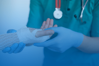 Profissional médico aplicando bandagem na mão lesionada de um paciente, representando assistência em benefício acidentário em Itapetininga.